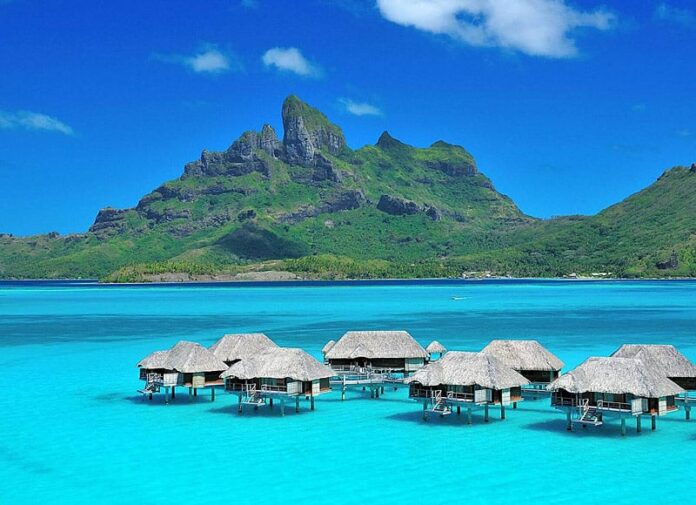 Overwater bungalows at the Four Seasons Resort with clear blue lagoon water and Mt. Otemanu in the background.